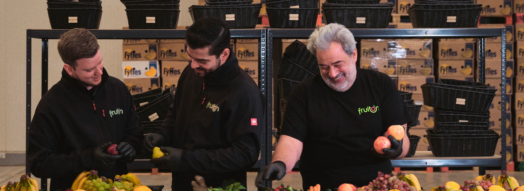 Drei Männer von fruiton stehen um einen Tisch voller Obst und genießen eine entspannte Gesprächsrunde.