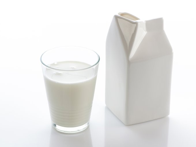 Ein Glas Milch steht neben einem Milchkarton auf dem Tisch, bereit für die Kaffeekultur am Arbeitsplatz.