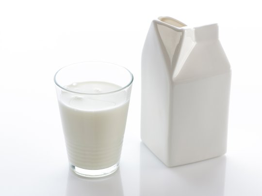 Ein Glas Milch steht neben einem Milchkarton auf dem Tisch, bereit für die Kaffeekultur am Arbeitsplatz.