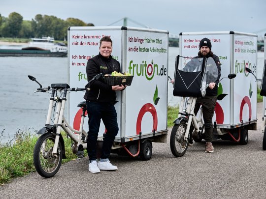 Zwei Personen auf Lasten-Fahrrädern, die das Konzept der nachhaltigen Lieferung und frische Produkte repräsentieren.